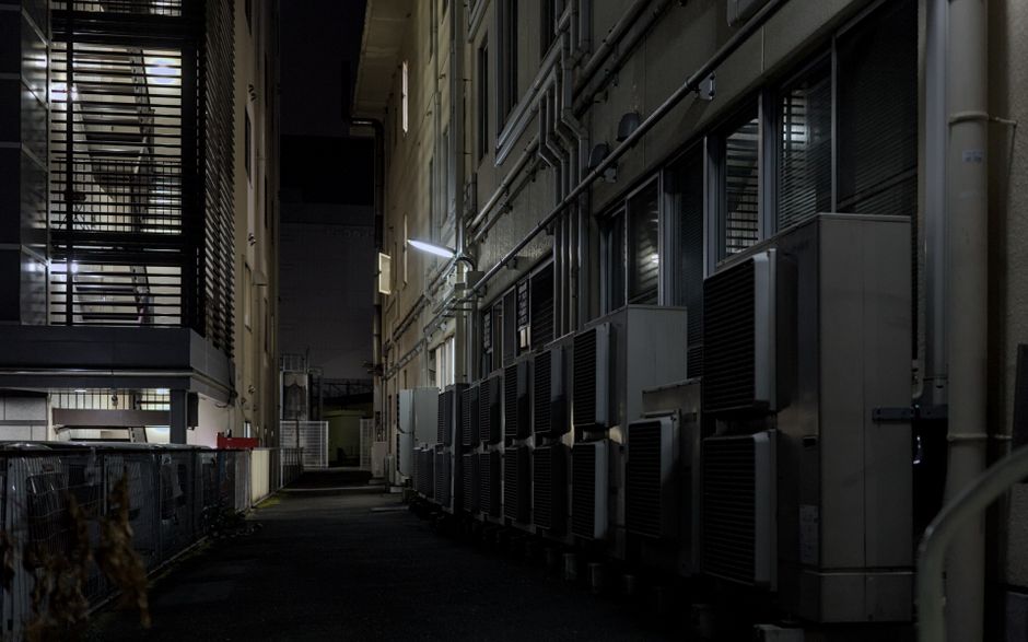 Corredor externo de um prédio com unidades de ar condicionado, ilustrando a infraestrutura de suporte às operações empresariais durante a noite.