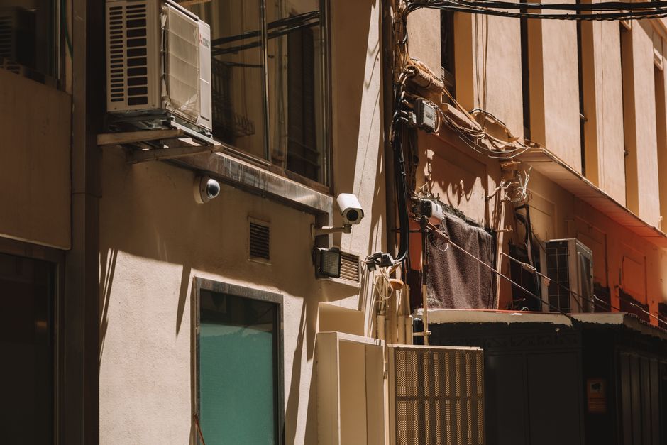 Imagem de uma fachada de edifício residencial ao pôr do sol, destacando detalhes arquitetônicos e elementos de ar condicionado e instalação elétrica.