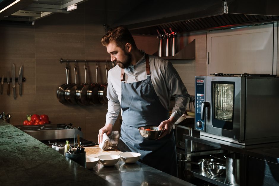 Homem preparando uma receita na cozinha de um restaurante, demonstrando cuidado na organização e na cozinha profissional.