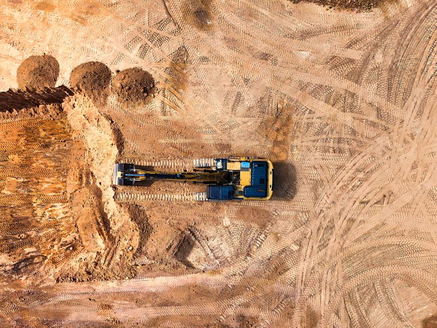 Imagem aérea de uma escavadeira trabalhando em um terreno de terra, ilustrando atividades de construção ou mineração.