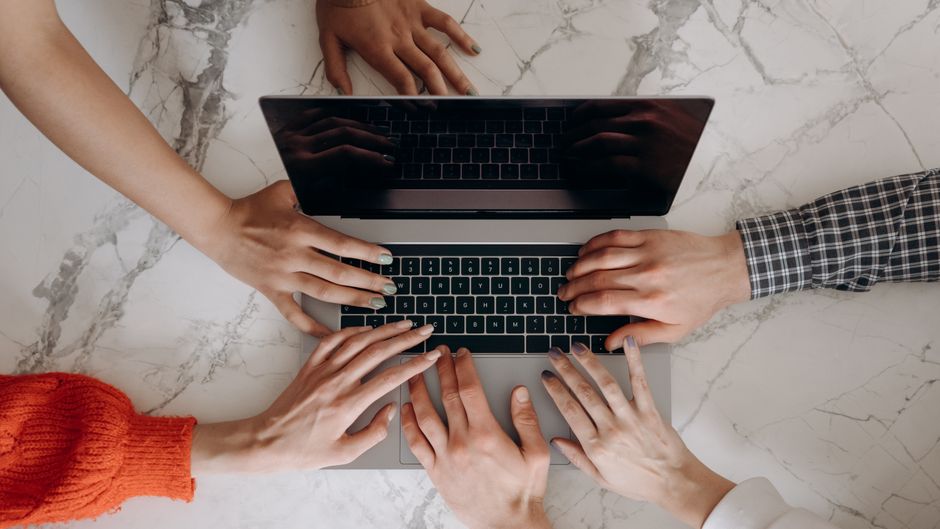 Grupo de pessoas colaborando em um projeto digital usando um laptop em um ambiente de escritório moderno.