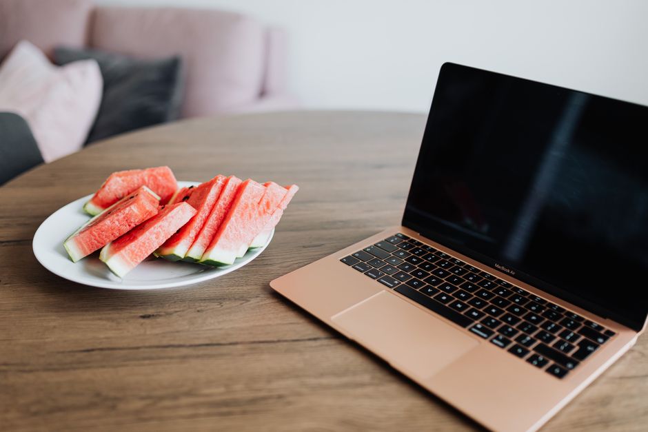 Imagem de um ambiente de trabalho doméstico com um laptop e uma placa de fatias de melancia, ideal para um artigo sobre equilíbrio entre trabalho e lazer na rotina remota.