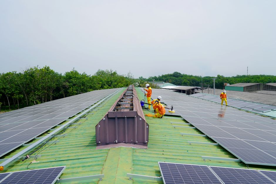Técnicos instalando painéis solares em um telhado de ferro em uma área industrial, promovendo energia sustentável e inovação tecnológica.