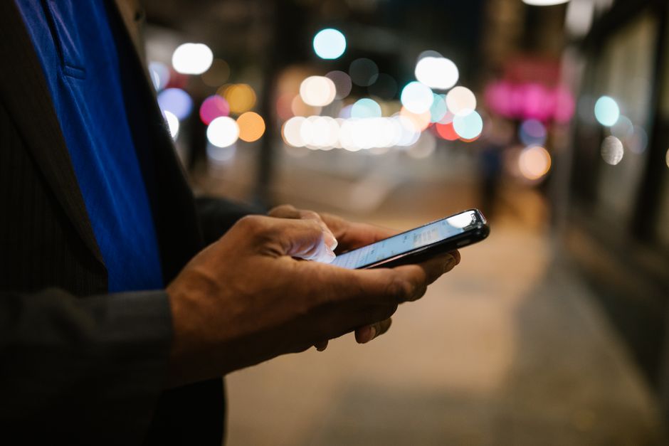 Homem usando um smartphone à noite, com foco na tecnologia e comunicação digital em ambientes urbanos.
