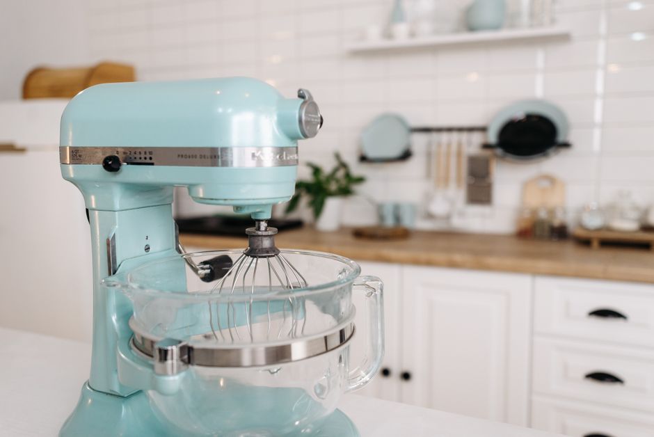 Foto de um misturador de cozinha de cor verde menta em um ambiente moderno, com fundo de pia, utensílios e decoração minimalista.