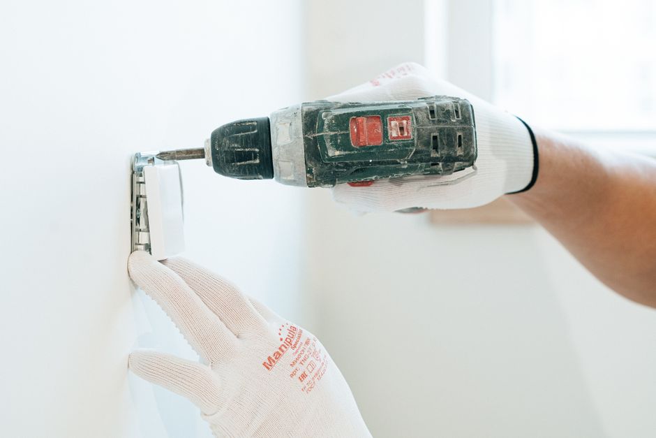 Pessoa usando parafusadeira elétrica para fixar uma prateleira na parede, representando melhorias na estrutura de um ambiente interno.