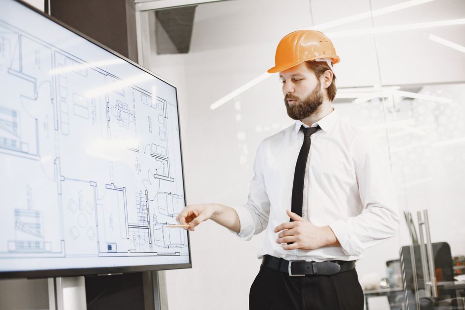 Profissional de engenharia analisando um projeto arquitetônico em uma sala de reunião moderna.