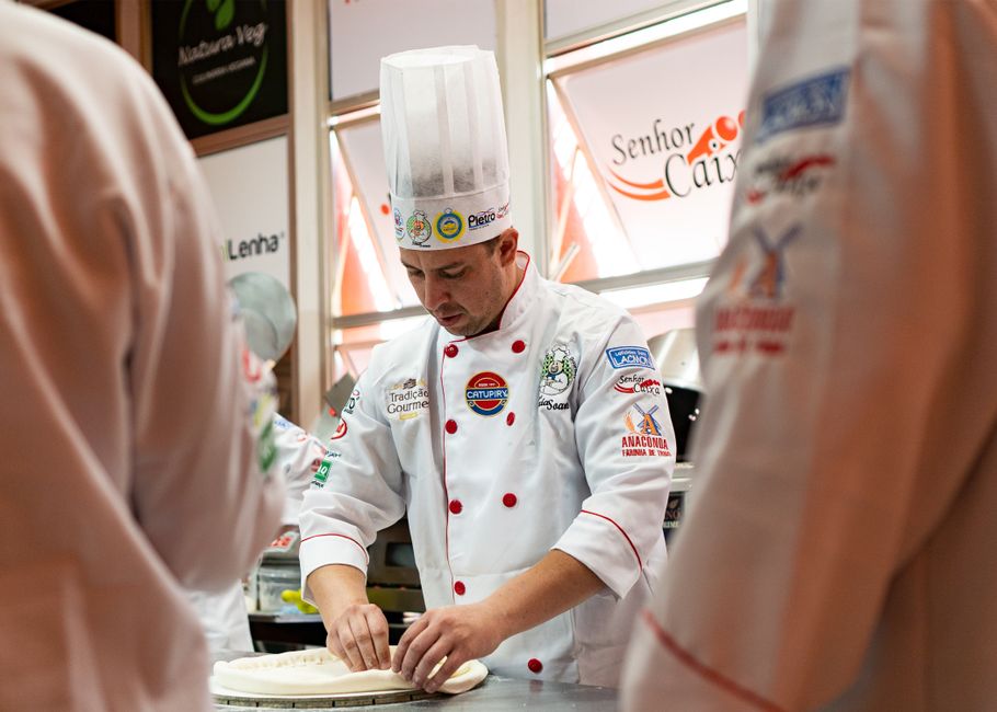 Chef confeitando massa em uma cozinha profissional, demonstrando técnica e cuidado na preparação culinária.