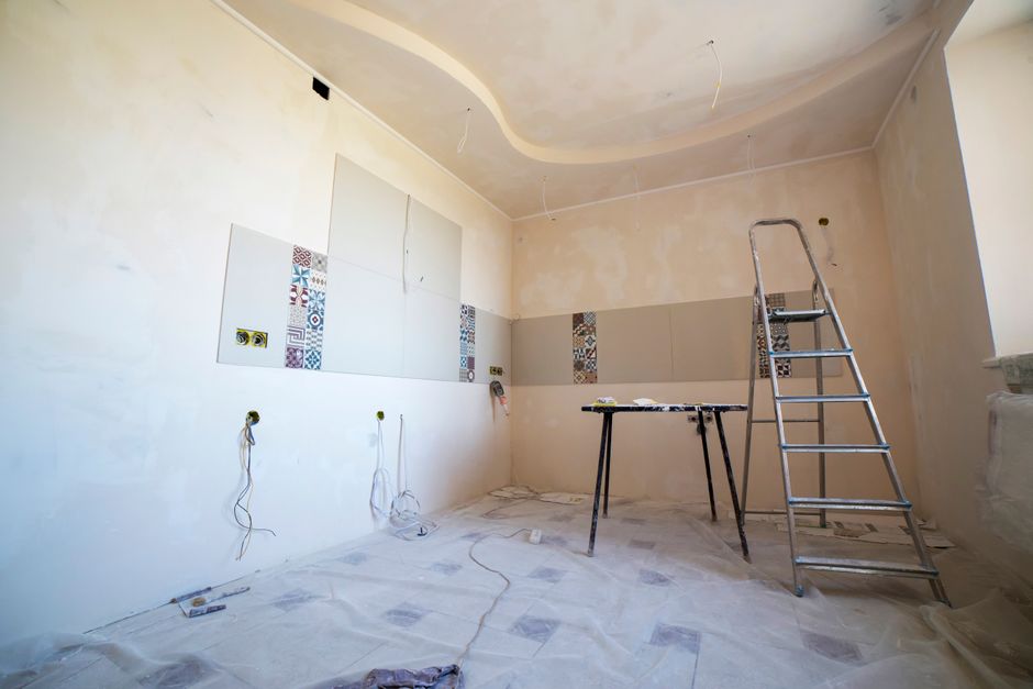 Imagem de uma sala em reforma, com paredes sendo preparadas para instalação de revestimentos e iluminação pendente.