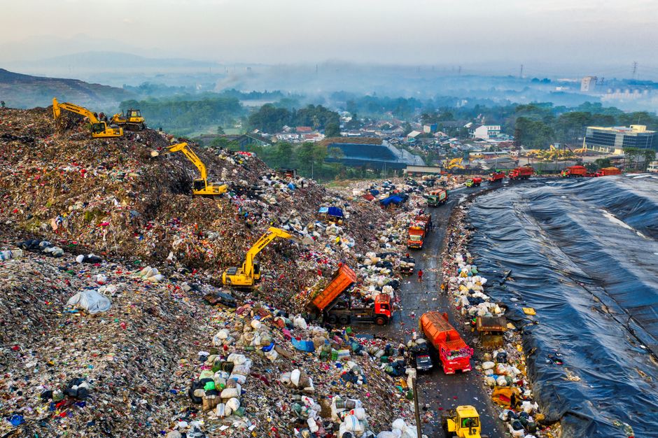 Imagem de um aterro sanitário com caminhões de lixo e tratores em operação, representando gestão de resíduos sólidos e sustentabilidade.