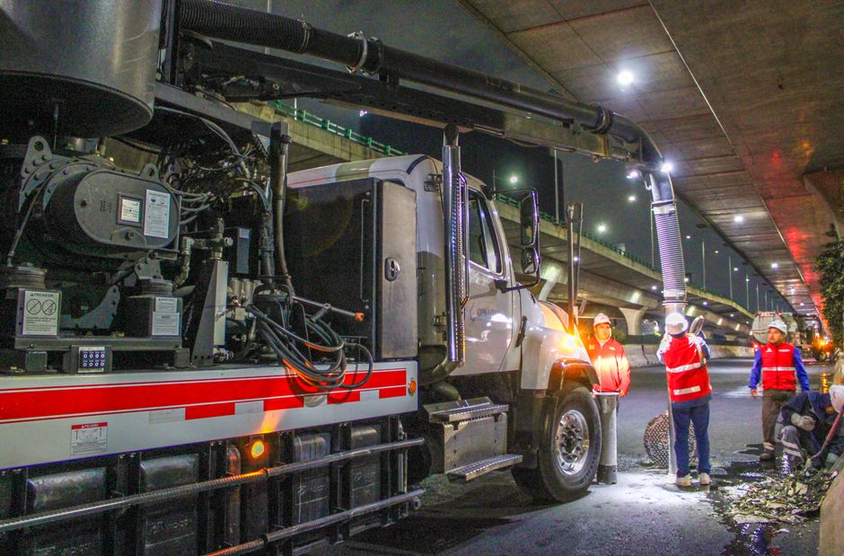 Equipe de trabalhadores realizando manutenção ou inspeção em uma infraestrutura de transporte sob um viaduto à noite.