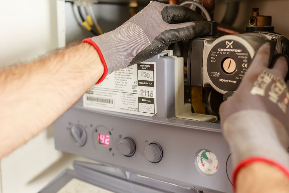 Técnico de manutenção ajustando um aquecedor de água, demonstrando reparo técnico e inspeção de equipamentos.