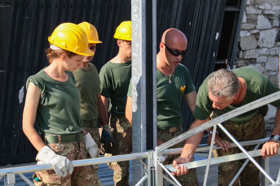 Grupo de trabalhadores em uniforme militar participando de uma atividade de inspeção ou construção ao ar livre, demonstrando coordenação e atenção aos detalhes.