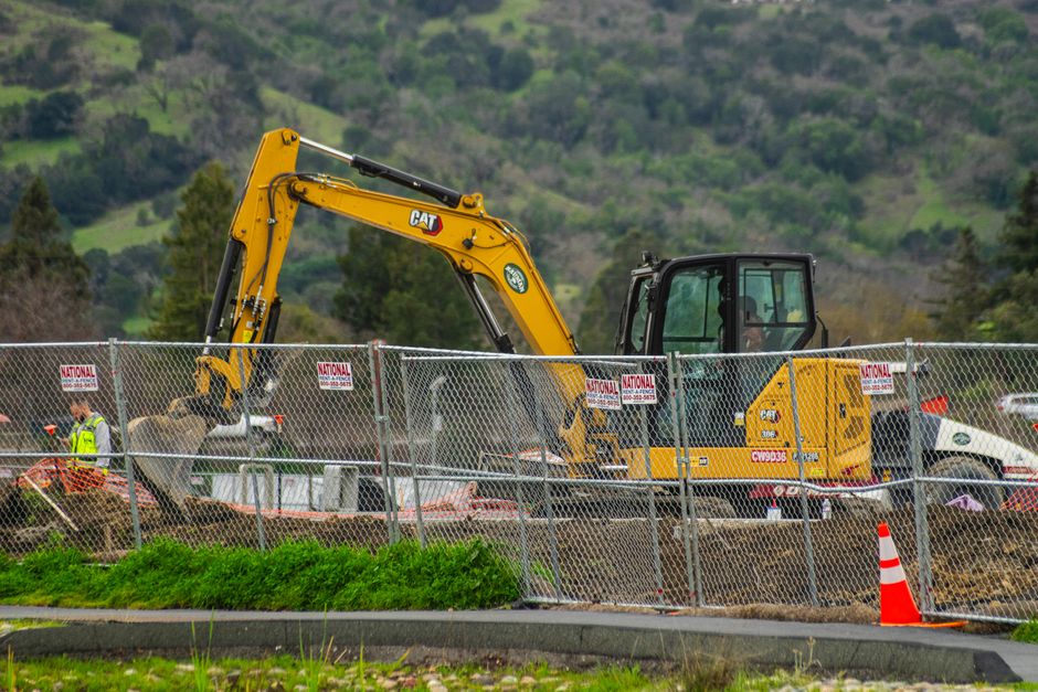 Máquina de escavação trabalhando em canteiro de obra com paisagem ao fundo, representando construção civil e infraestrutura.