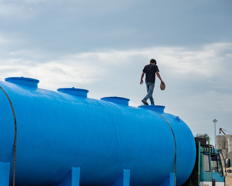 Homem caminhando na parte superior de um grande tanque de armazenamento azul, representando segurança e controle de processos industriais.