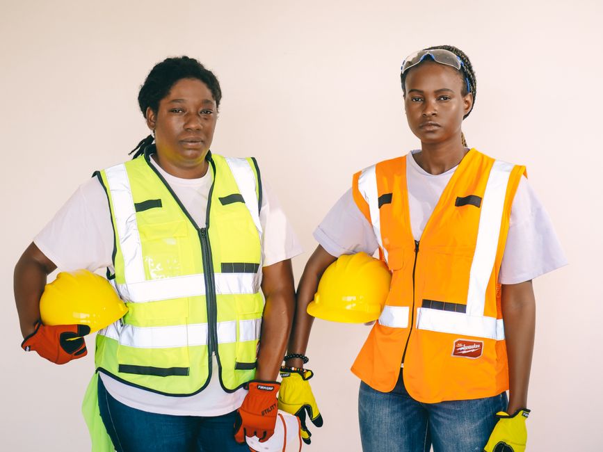 Duas mulheres profissionais de construção civil segurando capacetes, vestindo coletes de segurança, representando a força feminina na engenharia e obras.