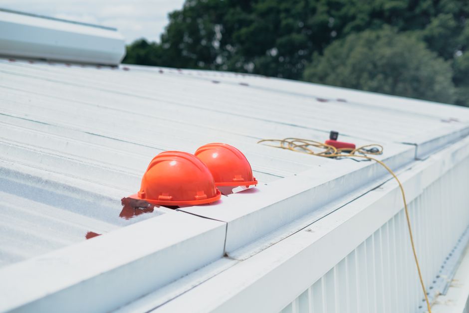 Imagem de dois capacetes de segurança instalados no telhado de uma construção metálica, indicando inspeção ou manutenção predial.