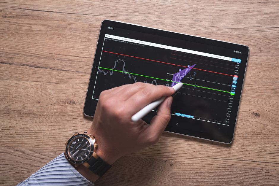 Pessoa analisando gráficos de mercado financeiro em um tablet com caneta digital, destaque para tendências de investimento e ações de mercado.