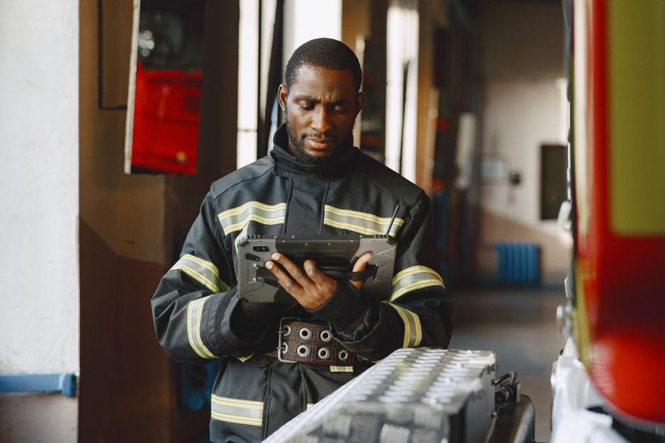 Bombeiro avaliando dados em um dispositivo portátil dentro de uma estrutura de operacionais de emergência.
