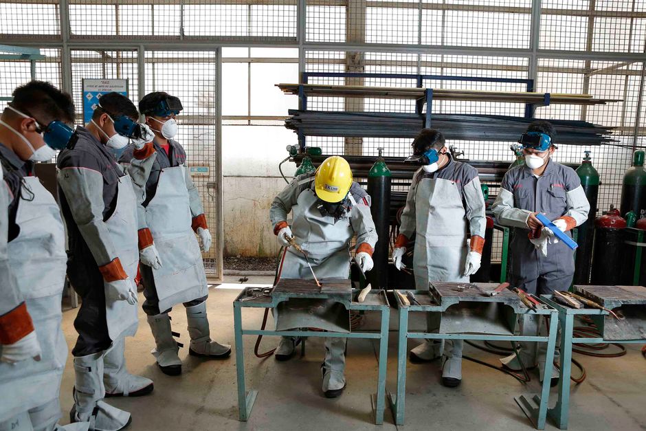 Grupo de trabalhadores em um ambiente industrial realizando treinamento ou demonstração de procedimentos de soldagem com equipamentos de segurança adequados.