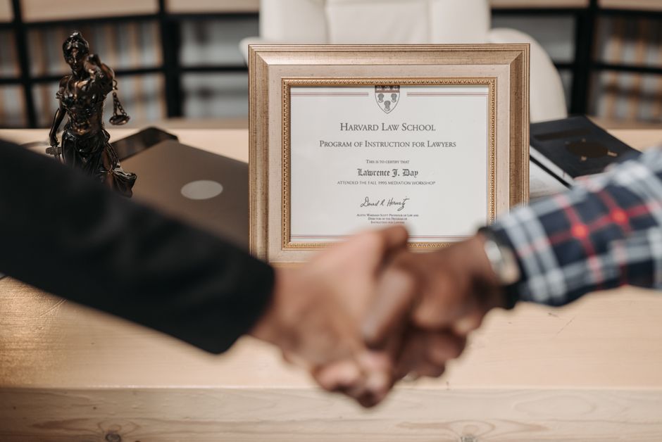Imagem de duas pessoas fechando um acordo em um ambiente profissional, com um diploma da Harvard Law School ao fundo, simbolizando parceria ou sucesso acadêmico.