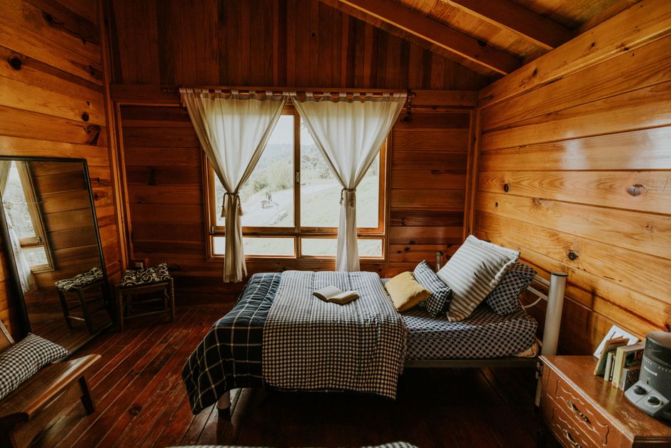 Quarto rústico de madeira com cama feita e janelas que revelam uma paisagem natural ao fundo.
