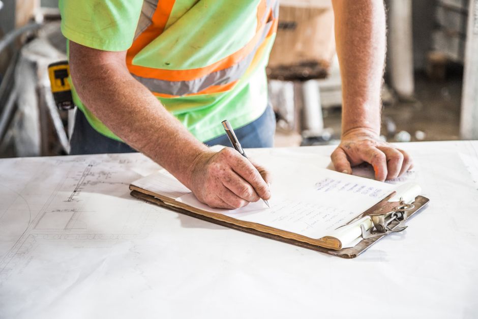 Homem anotando planos ou relatórios em uma obra de construção, focando na gestão de projetos de construção civil.