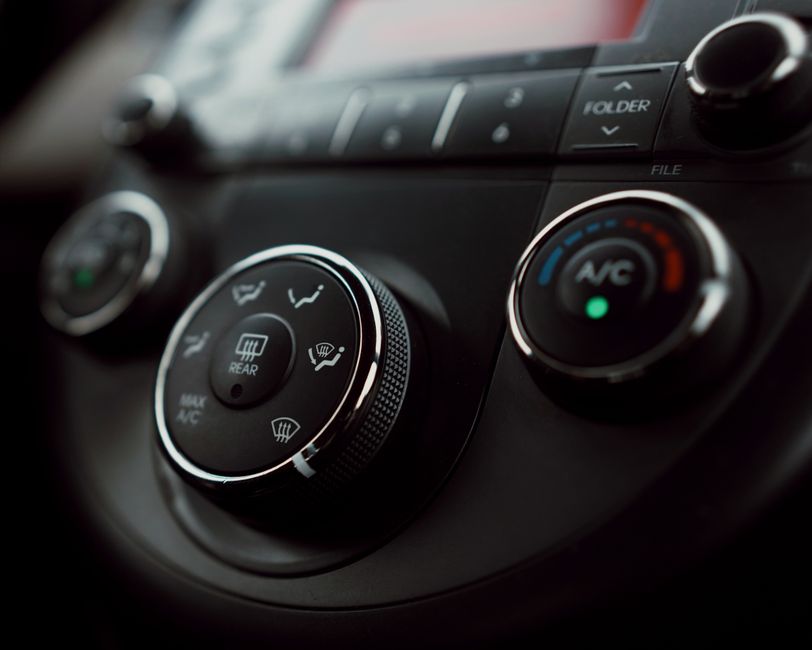 Imagem de um painel de controle de ar-condicionado de carro, focando nos botões e reguladores para clima e ventilação.