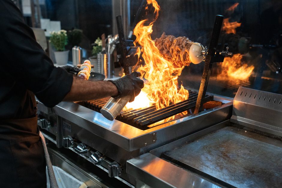 Chef profissional flambando um prato na cozinha, com destaque para a chama e a técnica de culinária com fogo.
