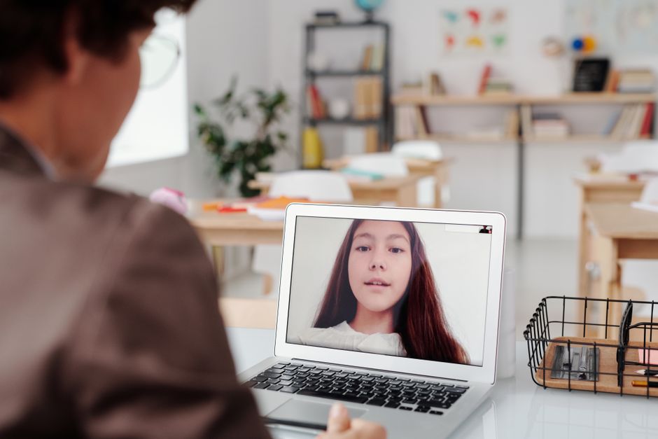 Professora participando de aula online com estudante, em ambiente de sala de aula adaptada para ensino remoto