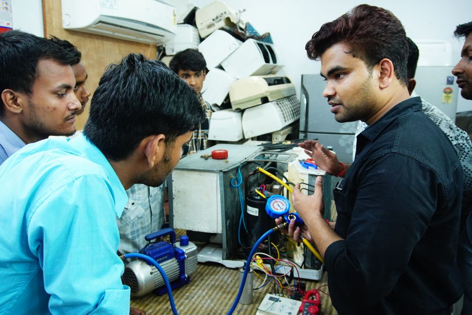 Grupo de jovens profissionais realizando aula prática de eletrônica ou manutenção de equipamentos eletrônicos em um ambiente de laboratório.