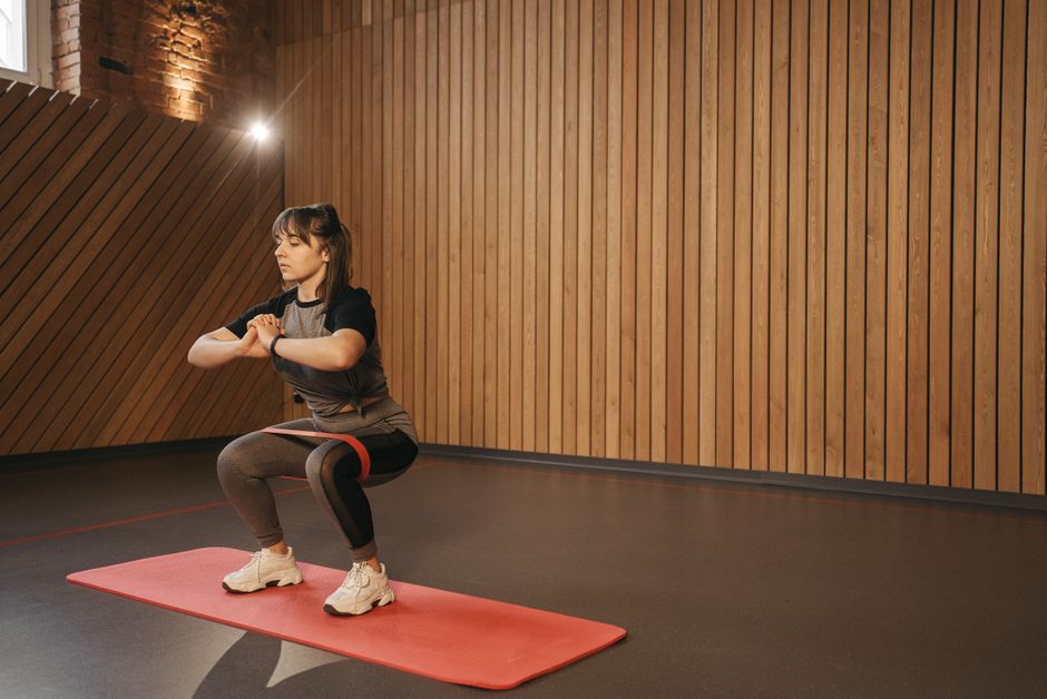 Mulher fazendo exercício de agachamento em academia com paredes de madeira, illustrating bem-estar e fitness.