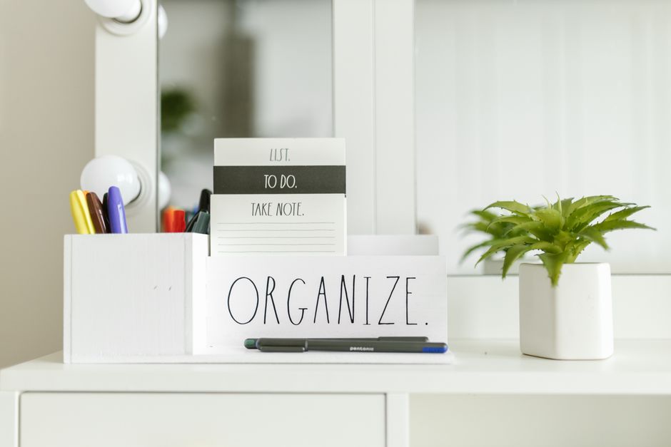 Imagem de uma mesa bem organizada com itens de papelaria, um quadro motivacional e uma planta, transmitindo a ideia de organização e produtividade para um ambiente de trabalho ou estudo.