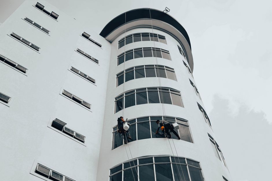 Equipe de trabalhadores realizando limpeza de janelas em edifício moderno de alto padrão.
