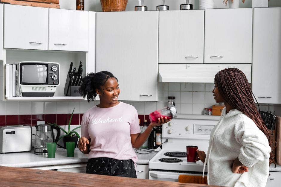 Duas mulheres conversando e compartilhando um momento de convivência na cozinha, demonstrando amizade e interação social.