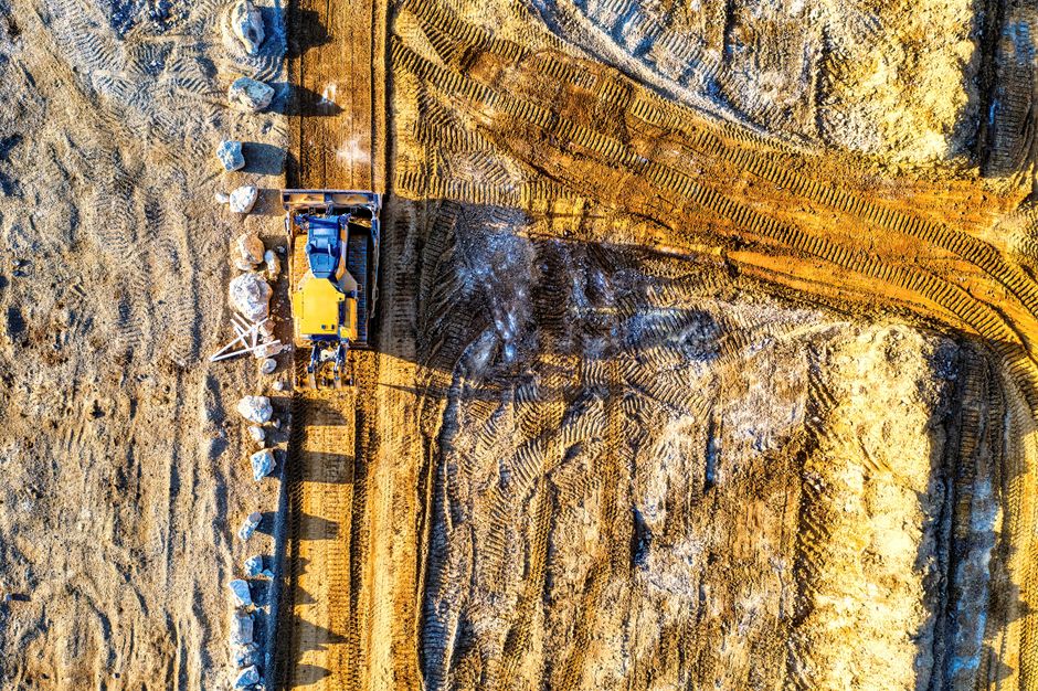 Imagem aérea de uma obra de terraplenagem com máquinas e marcas no solo, ilustrando construção civil e avanço de projetos de infraestrutura.