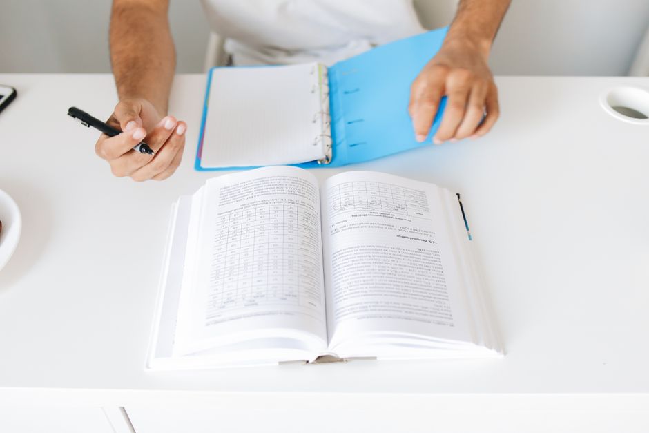 Pessoa estudando e analisando dados financeiros em uma mesa de trabalho com livros e caderno.