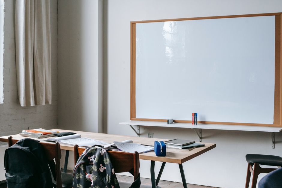 Imagem de uma sala de aula ou sala de treinamento com duas mesas e uma lousa branca, sugerindo um ambiente de estudo ou capacitação.