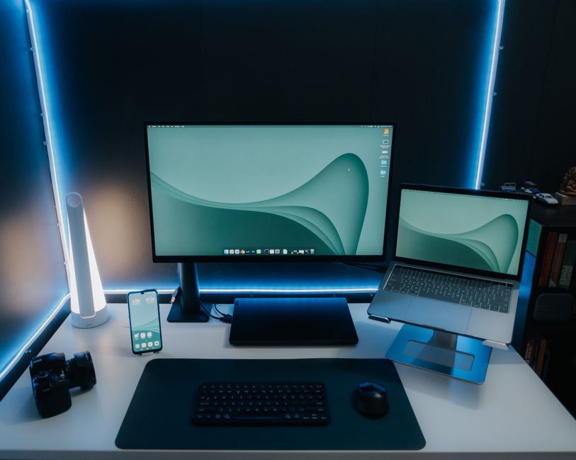 Imagem de uma estação de trabalho moderna com dois monitores, teclado, mouse, smartphone, e iluminação de LED azul, ideal para temas relacionados à tecnologia, produtividade e home office.