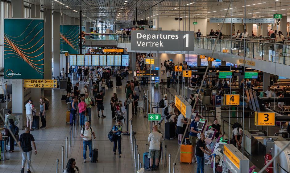 Imagem de um saguão de aeroporto com diversos passageiros, balcões de check-in e telas de voos, representando viagens aéreas e mobilidade.