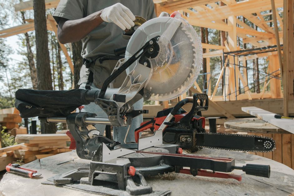 Homem operando uma serra circular em uma construção de madeira ao ar livre, destacando o trabalho na área de carpintaria ou construção civil.