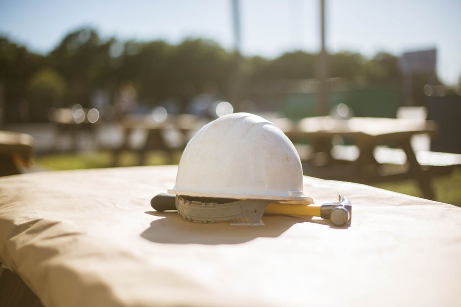 Foto de capacete de construção e martelo sobre uma mesa ao ar livre, simbolizando segurança no trabalho e obras civis.