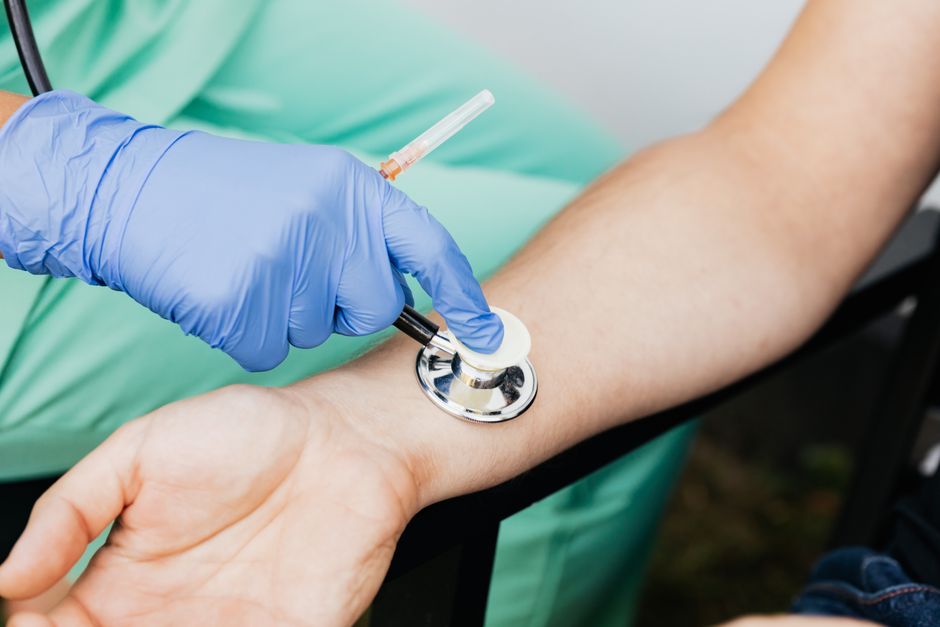 Profissional de saúde realizando uma coleta de sangue usando uma agulha e tubo de coleta, em ambiente clínico.