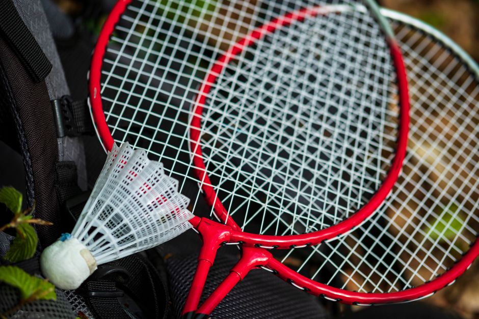 Imagem de duas raquetes de badminton ao lado de uma peteca, sugerindo esporte e lazer ao ar livre.