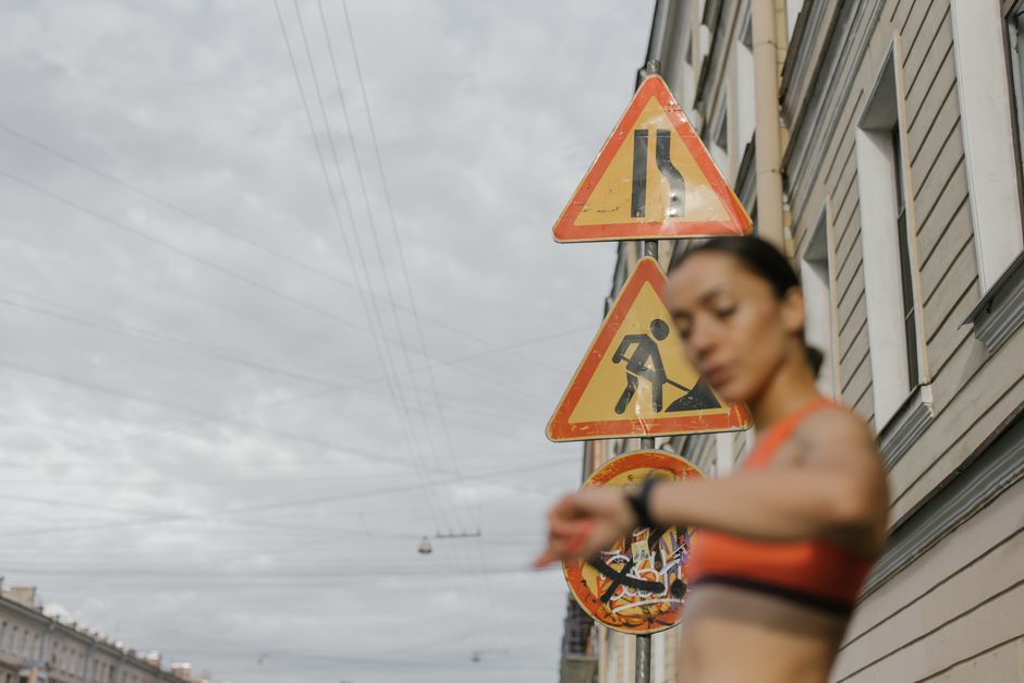 Mulher verificando o horário enquanto observa sinais de trânsito e obras na rua, simbolizando gerenciamento de tempo e atenção às mudanças.