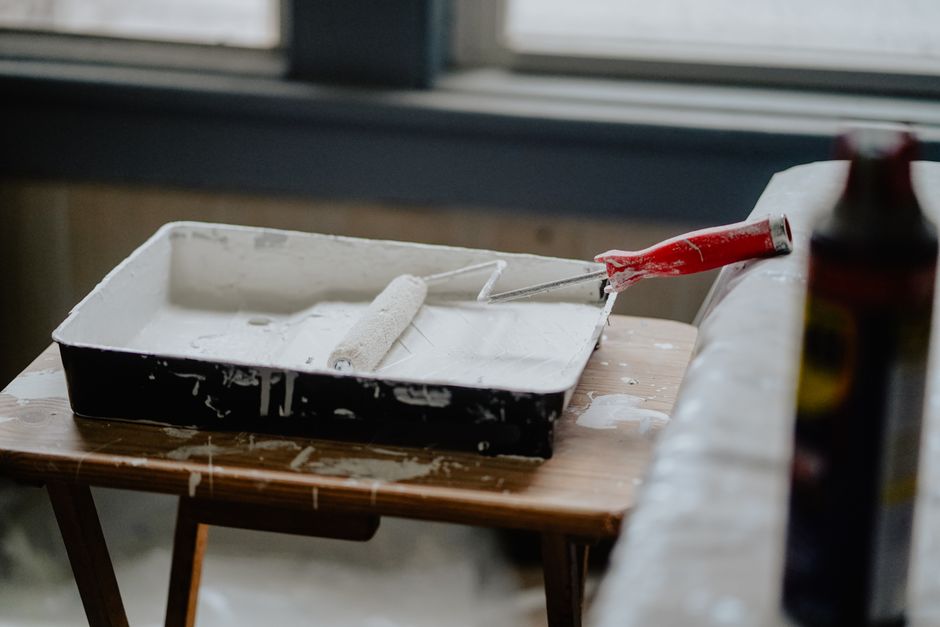 Pintura branca ainda fresca sobre uma bandeja, com um rolo de pintura e uma parede ao fundo, relacionado a projetos de renovação e decoração de interiores.