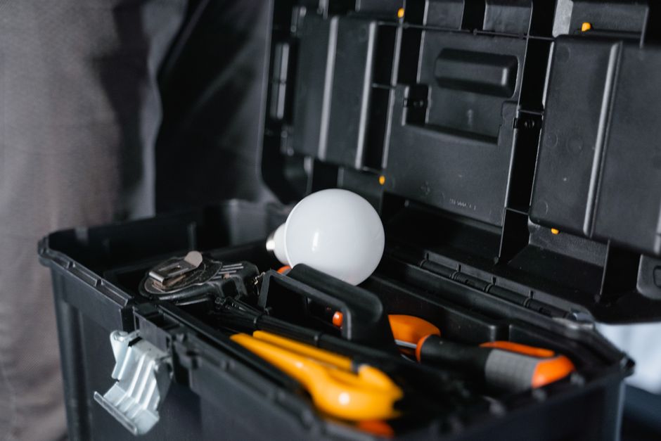 Imagem de uma caixa de ferramentas com uma lâmpada e outros utensílios, representando manutenção ou reparos em ambiente doméstico ou profissional.