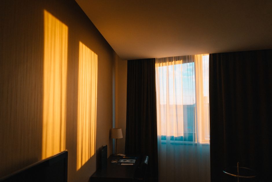 Luz natural entrando pela janela, criando sombras de iluminação na parede de um quarto durante o horário do pôr do sol ou amanhecer, transmitindo um ambiente tranquilo e acolhedor.