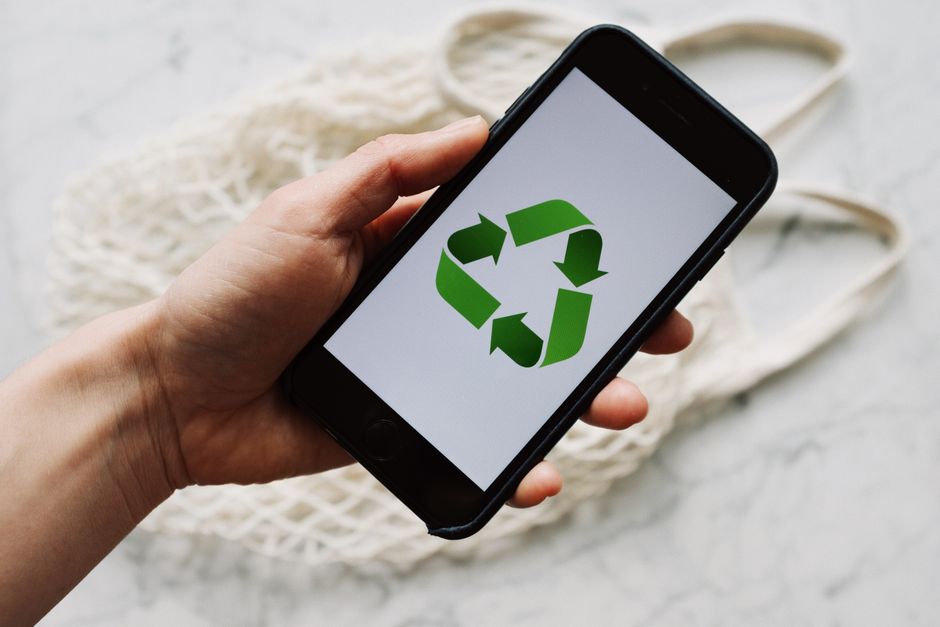 Pessoa segurando um smartphone com símbolo de reciclagem na tela, representando sustentabilidade e tecnologia.