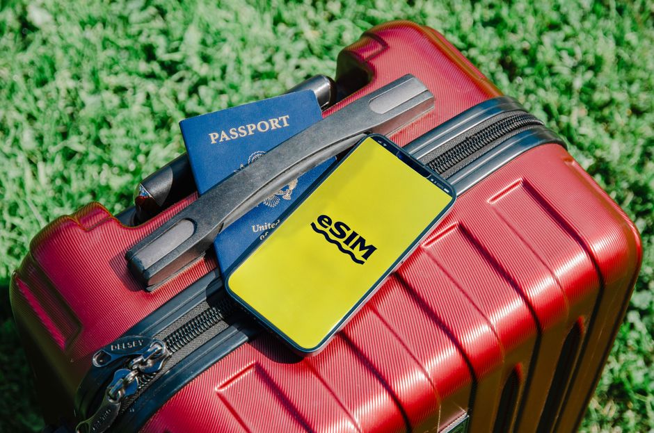 Imagem de uma mala de viagem com passaporte e smartphone exibindo a logo do aplicativo de transporte Sima, simbolizando planejamento de viagens ou negócios internacionais.